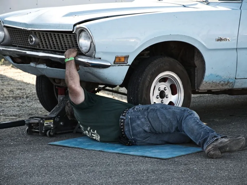 Bricoleur allongé sous une voiture surélevée, à l’atelier